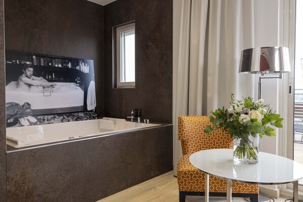 A modern bathroom with a large bathtub, a small window, and a round table with a vase of flowers. - Hotel de Castiglione (Paris)