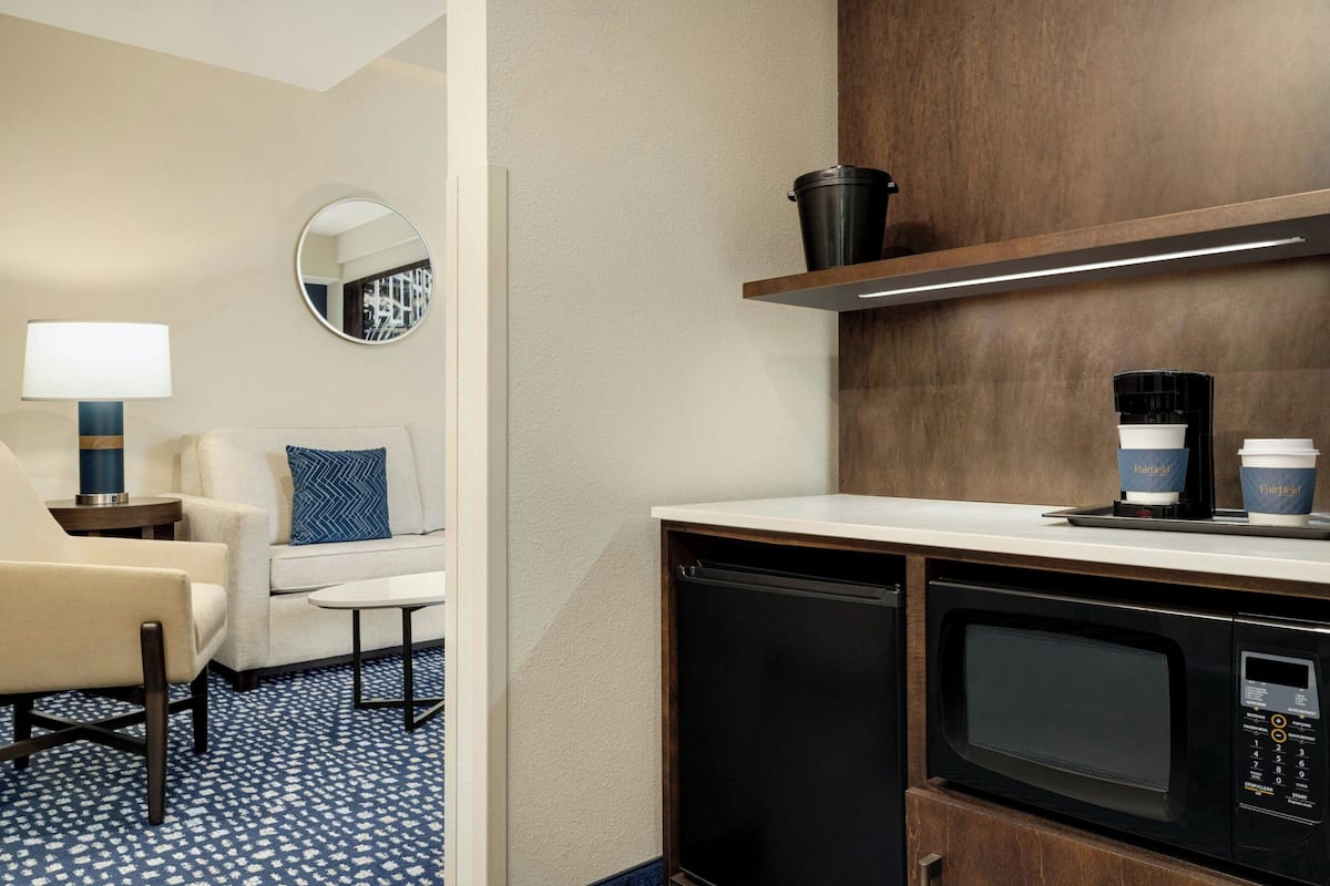 Habitación de hotel con sofá, sillón, cafetera, microondas y espejo.