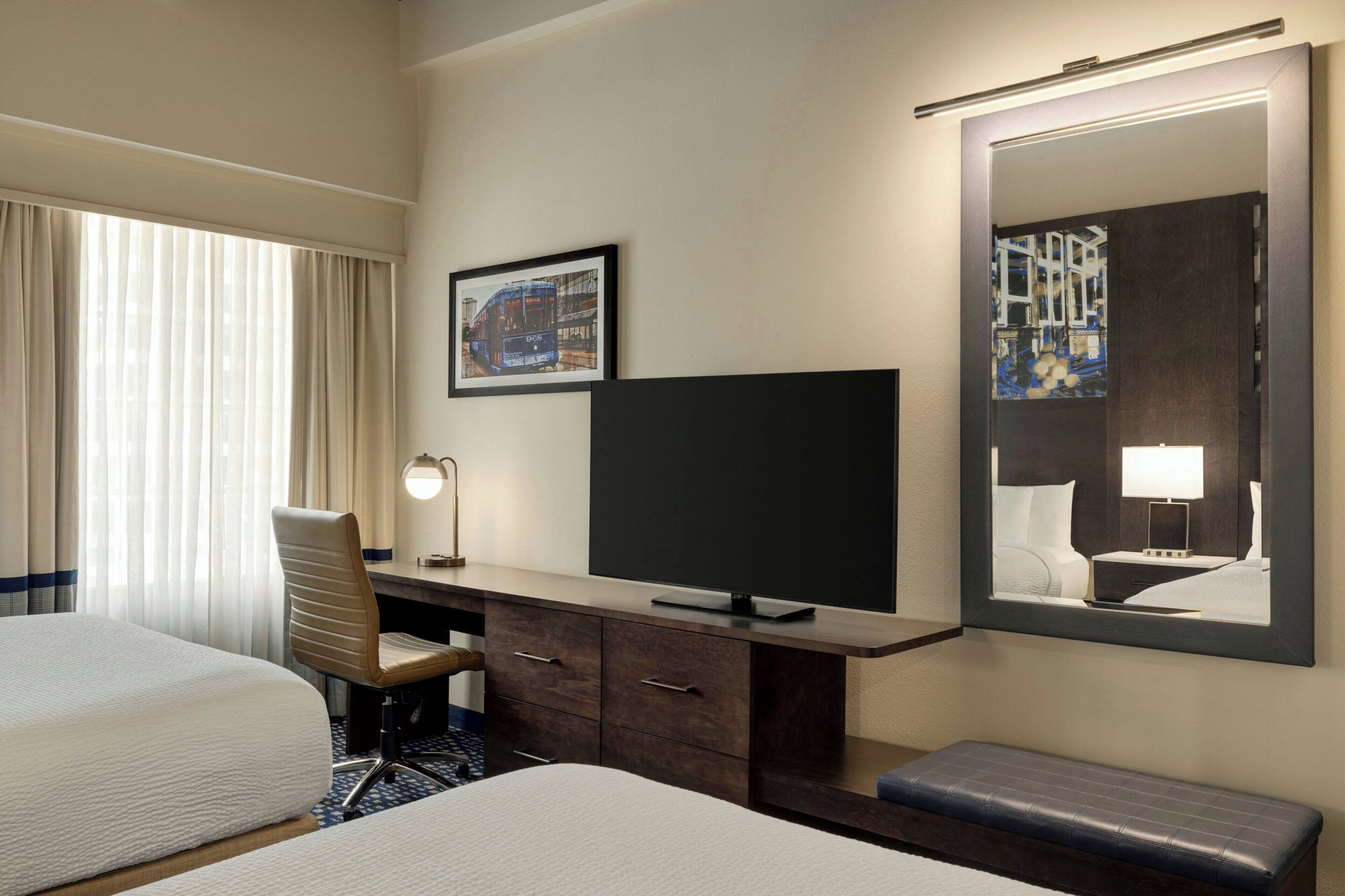 Une chambre d’hôtel avec deux lits, un bureau avec une chaise, une télévision et un grand miroir.
