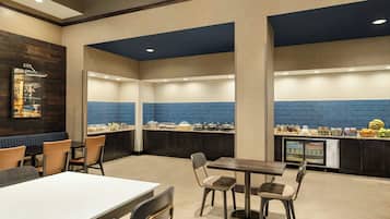 Un espace repas moderne avec une longue table et des chaises, un comptoir où sont présentés des aliments, et un mur recouvert de carreaux bleus.
