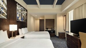 A hotel room with two beds, a desk, a television, and a large window with curtains.