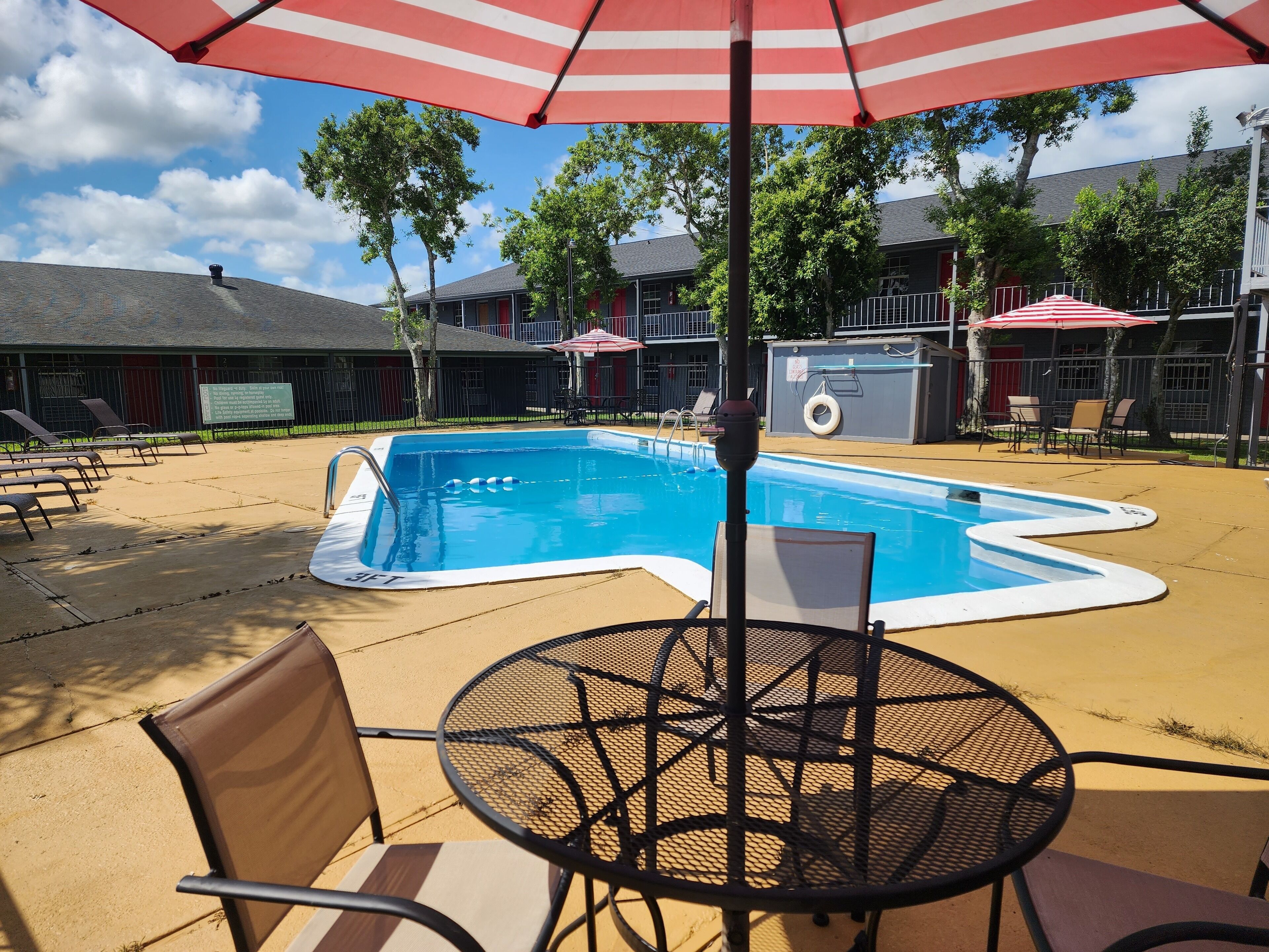 A swimming pool with a red and white striped umbrella, surrounded by lounge chairs and a table.