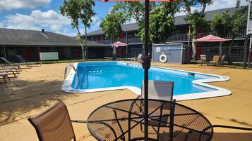 A swimming pool with a red and white striped umbrella, surrounded by lounge chairs and a table.