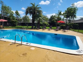 A swimming pool with lounge chairs and umbrellas, surrounded by trees and a fence.