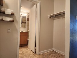 A bathroom with a toilet, sink, and mirror. There are towels on a shelf and a shower curtain rod.