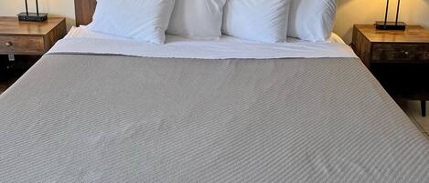 A neatly made bed with white linens and pillows, flanked by two bedside tables with lamps.