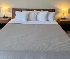 A neatly made bed with white linens and pillows, flanked by two bedside tables with lamps.