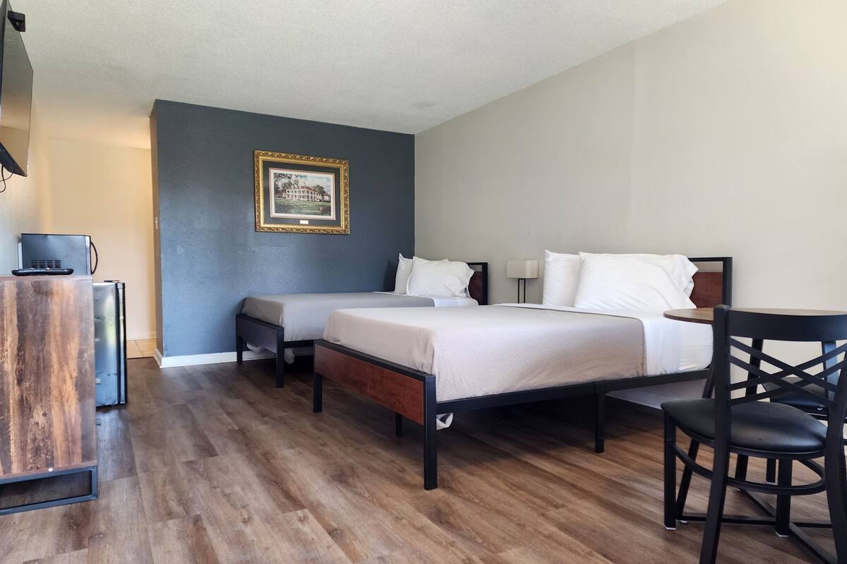 A hotel room with two beds, a desk, a chair, and a small refrigerator.