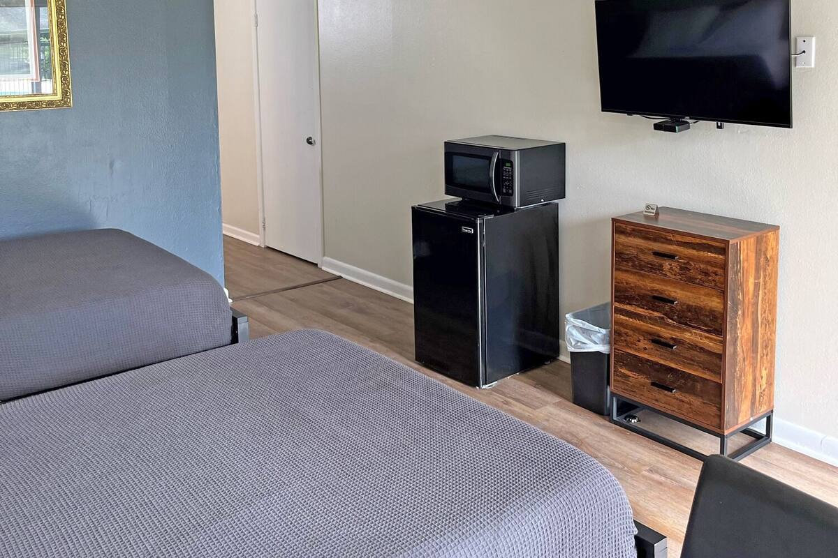 A room with two single beds, a microwave, a small refrigerator, a TV, and a wooden cabinet.