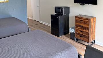 Habitación con dos camas individuales, microondas, refrigerador pequeño, televisión y un armario de madera.