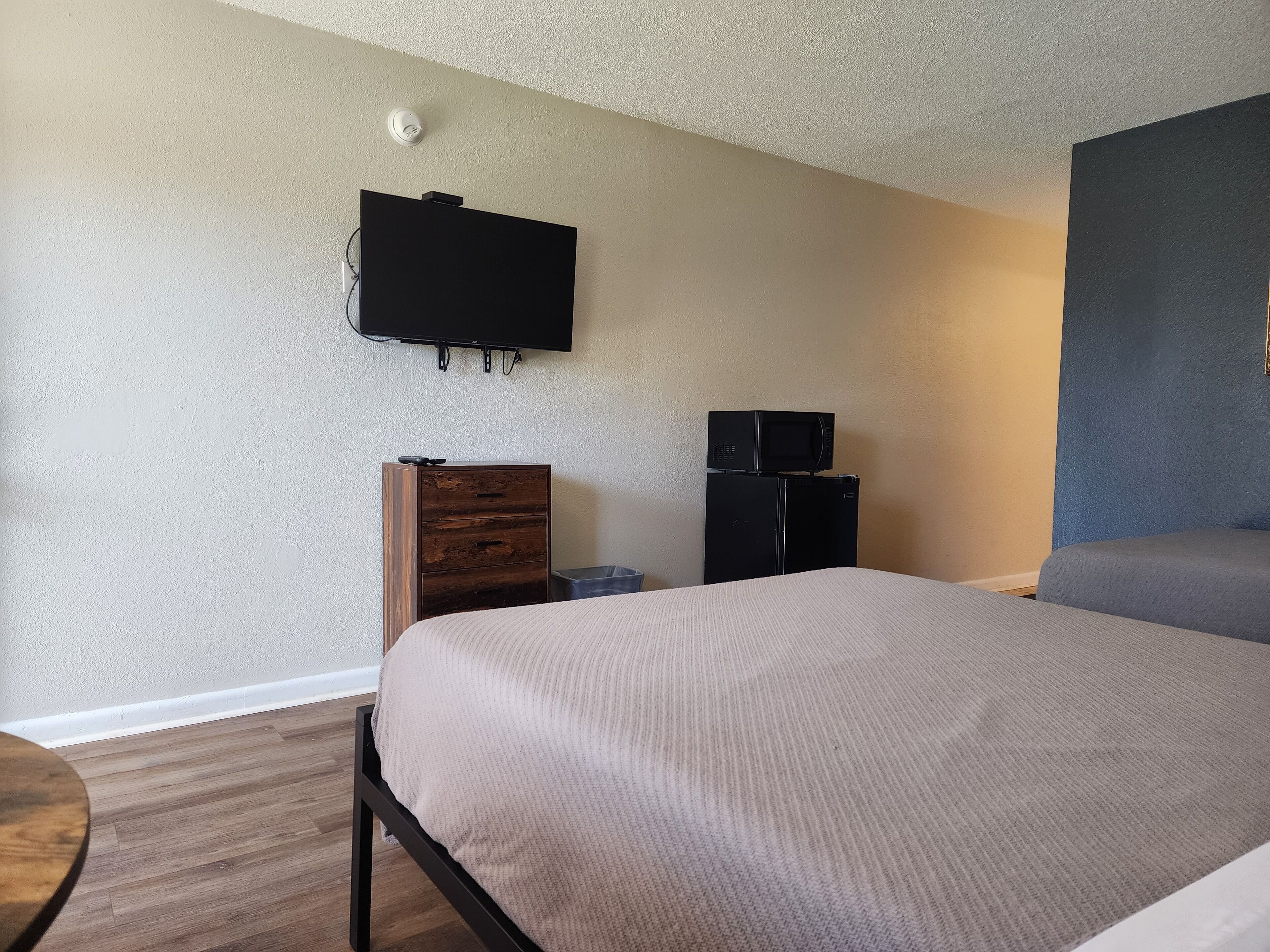 A hotel room with a bed, a dresser, a television mounted on the wall, and a refrigerator.