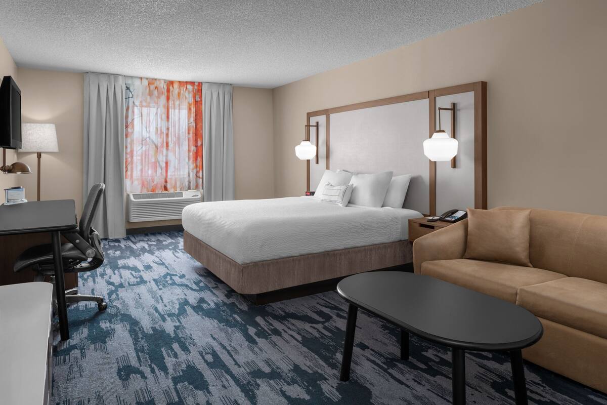 A hotel room with a bed, a desk, a chair, a sofa, and a TV.