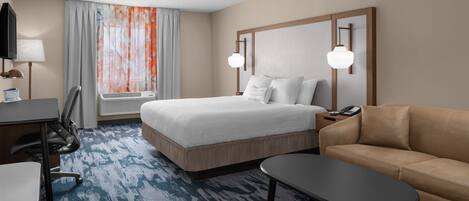 Una habitación de hotel con cama, escritorio, silla, sofá y televisión.