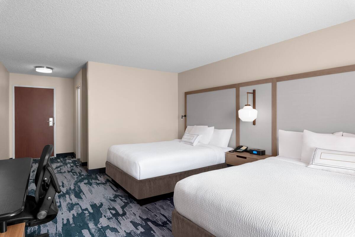 A hotel room with two beds, a desk, and a chair.
