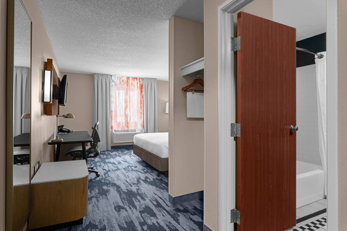 A hotel room with a bed, desk, chair, and a shower area.