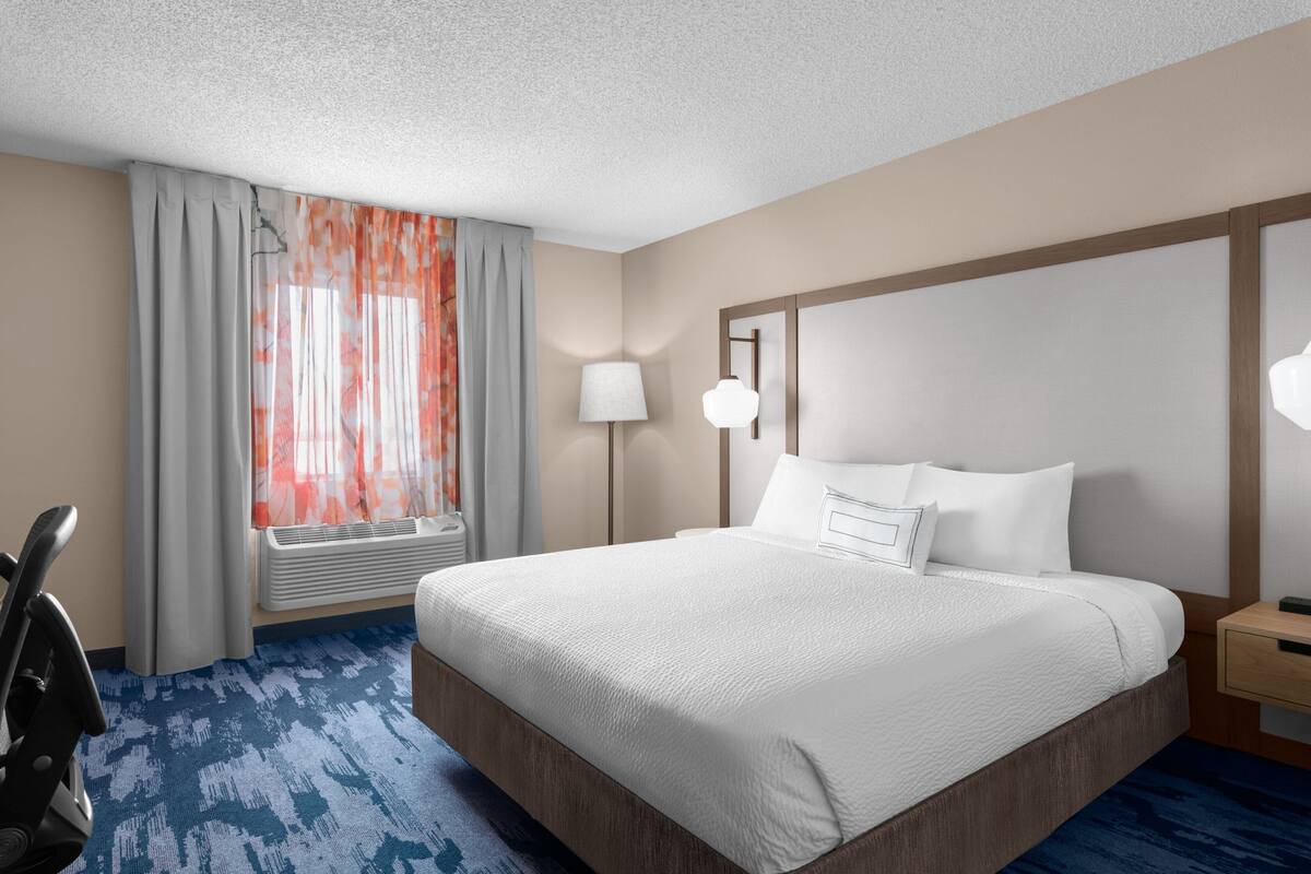 A hotel room with a large bed, a desk, a chair, a lamp, and a window with curtains.