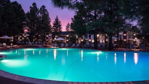 A swimming pool with lounge chairs and umbrellas, surrounded by trees and buildings.