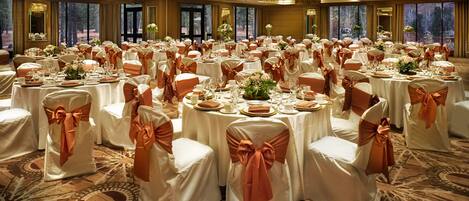 A banquet hall with round tables, white tablecloths, and chairs with orange sashes.