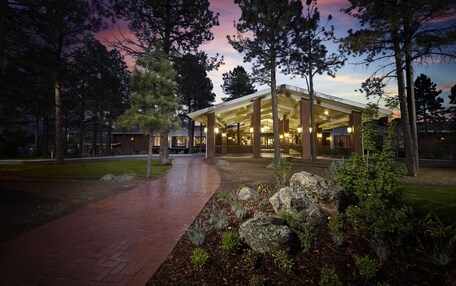 A modern building with a covered entrance, surrounded by trees and a landscaped area with rocks and plants.