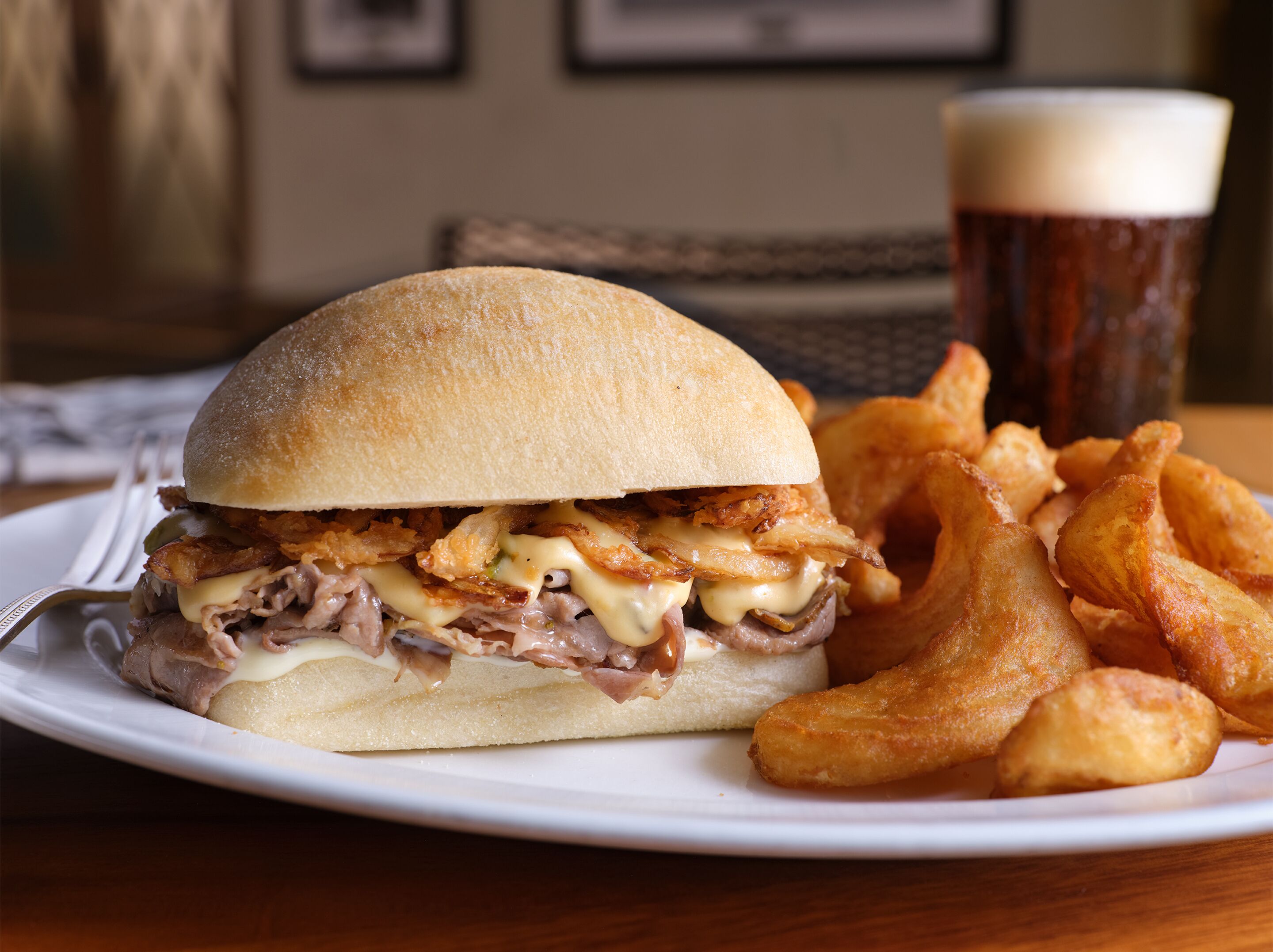 A plate with a sandwich and fries, and a glass of beer.