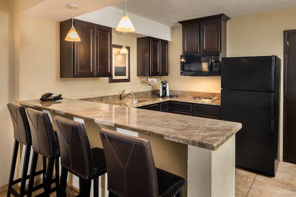 A kitchen with dark wooden cabinets, a black refrigerator, a marble countertop, and pendant lighting. - Holiday Inn Hotel & Suites Charleston West by IHG (South Charleston)