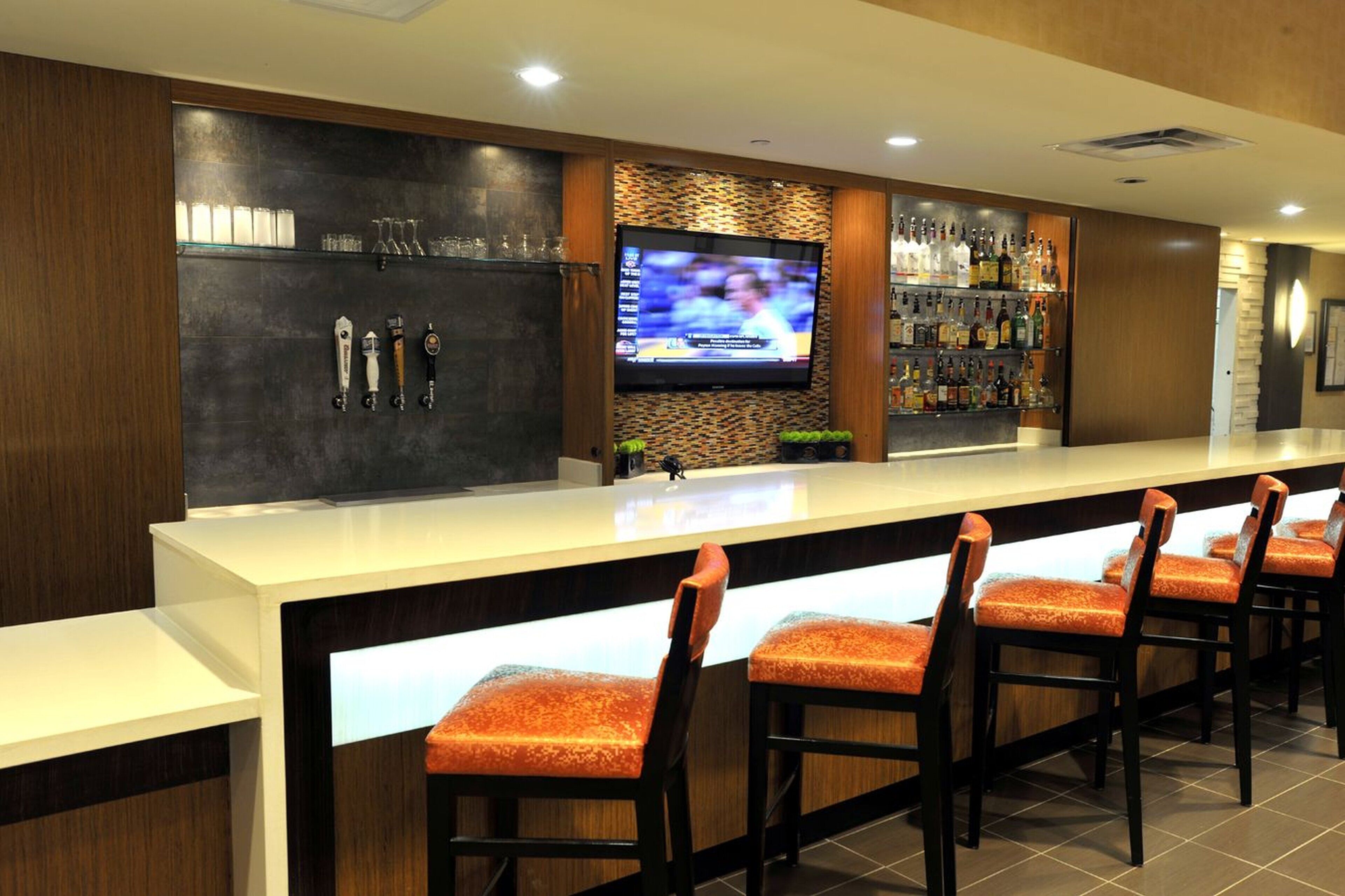 A bar area with a TV, bar stools, and a shelf of liquor bottles.