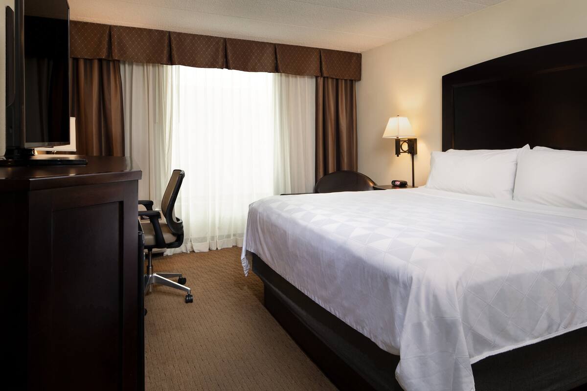 A hotel room with a large bed, a desk with a computer, a chair, and a lamp.