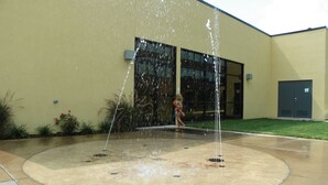 A water feature with multiple jets in a circular basin, surrounded by a paved area with a building in the background. - Holiday Inn Hotel & Suites Charleston West by IHG (South Charleston)