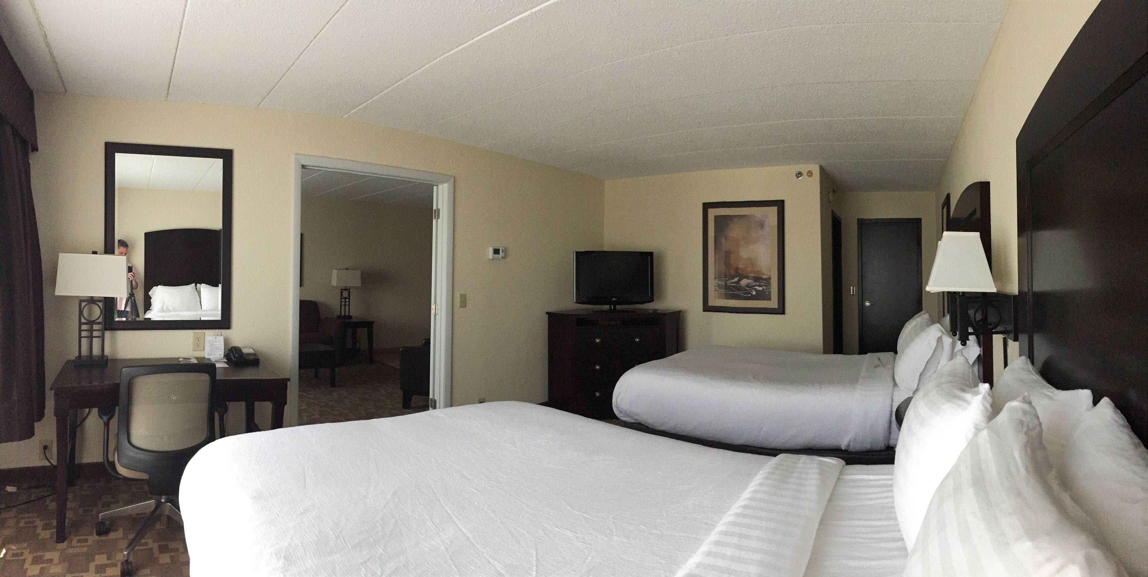A hotel room with two beds, a desk with a chair, a television, and a painting on the wall.