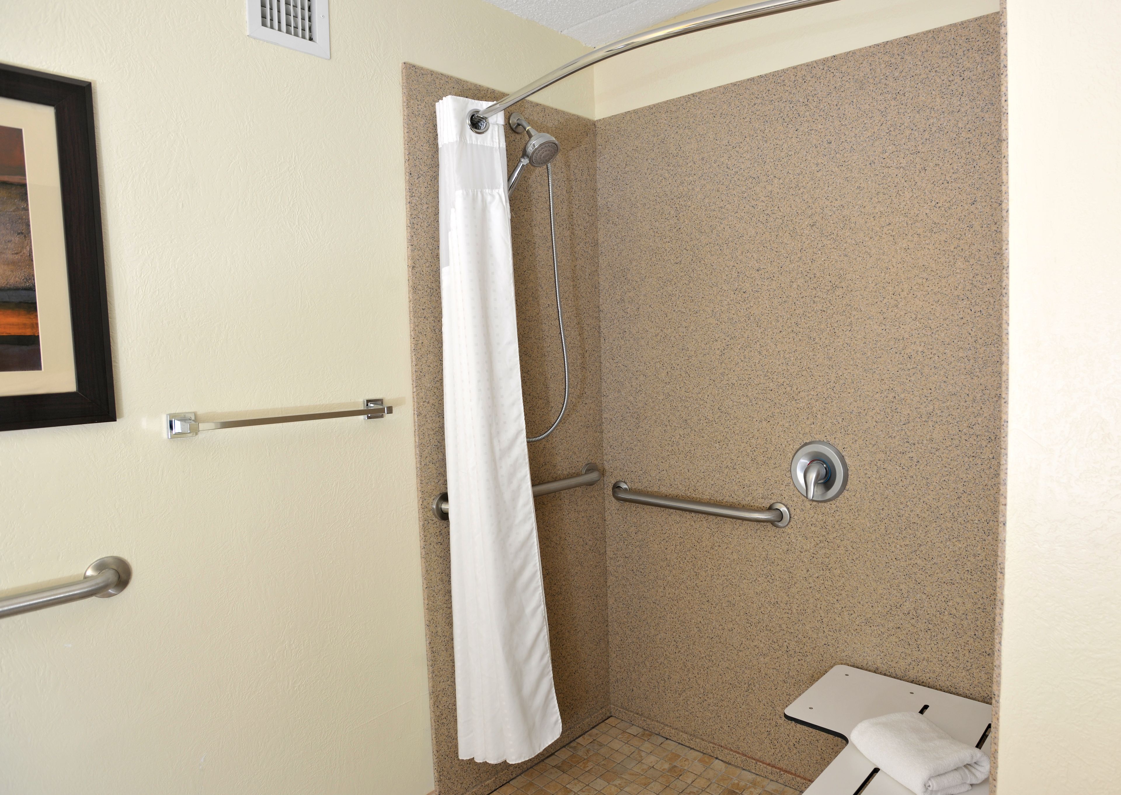 A shower with a white curtain, grab bars, and a handheld showerhead.