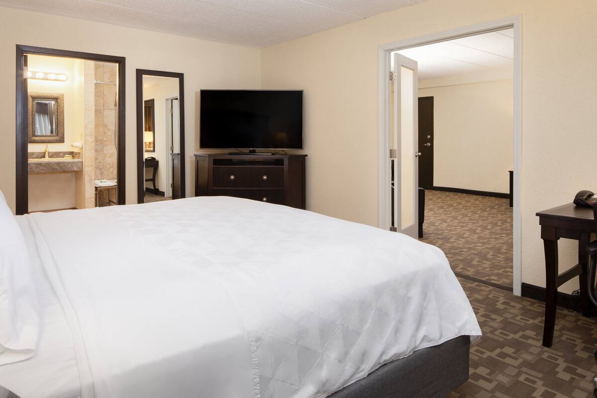 A hotel room with a large bed, a TV on a dresser, a mirror, and a bathroom visible through an open door.