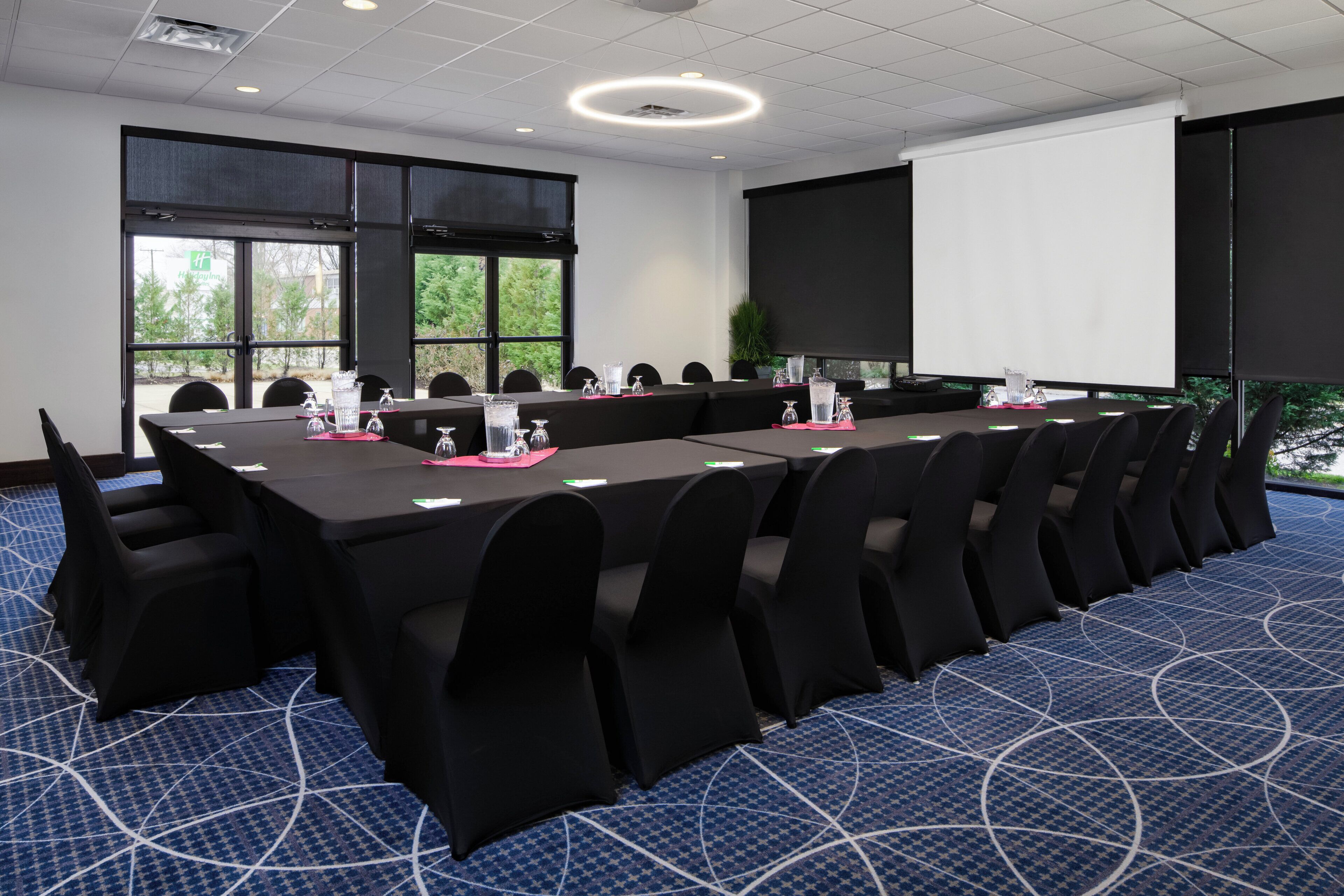 A conference room with a long table, chairs, and a projector screen.