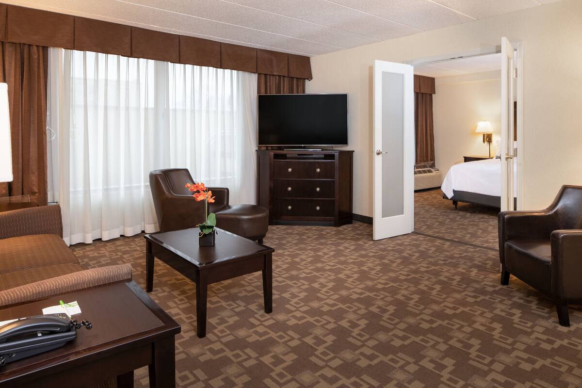 A hotel room with a large bed, a television, a desk with a telephone, and a chair.