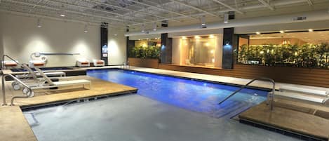 A swimming pool with a water slide, lounge chairs, and a reception area with plants.