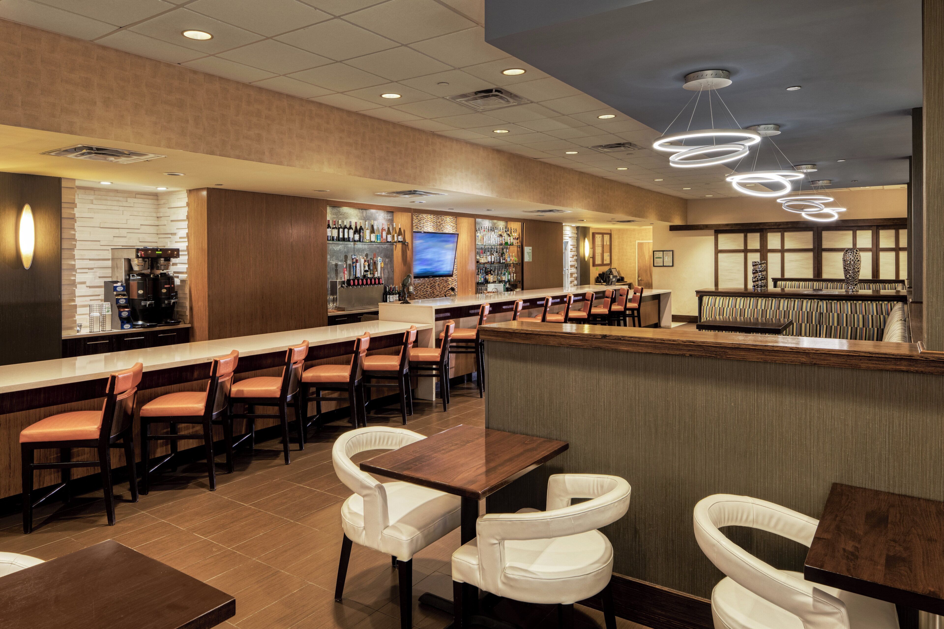 A bar area with multiple seating options, including bar stools and cushioned chairs, and a counter with a variety of bottles and glasses.