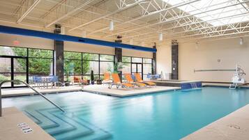 An indoor swimming pool with a clear view of the outside, lounge chairs, and a lifeguard stand.