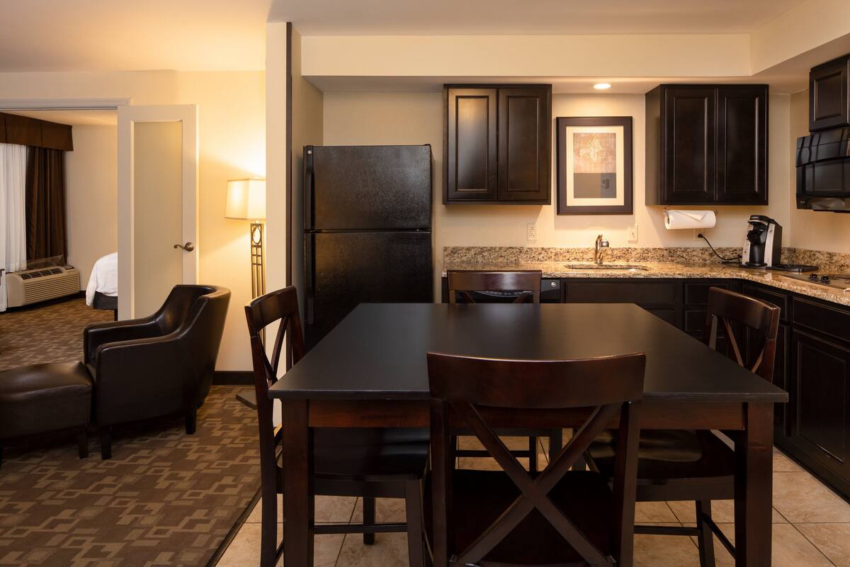 A hotel room with a dining area, a refrigerator, a coffee maker, and a lamp.