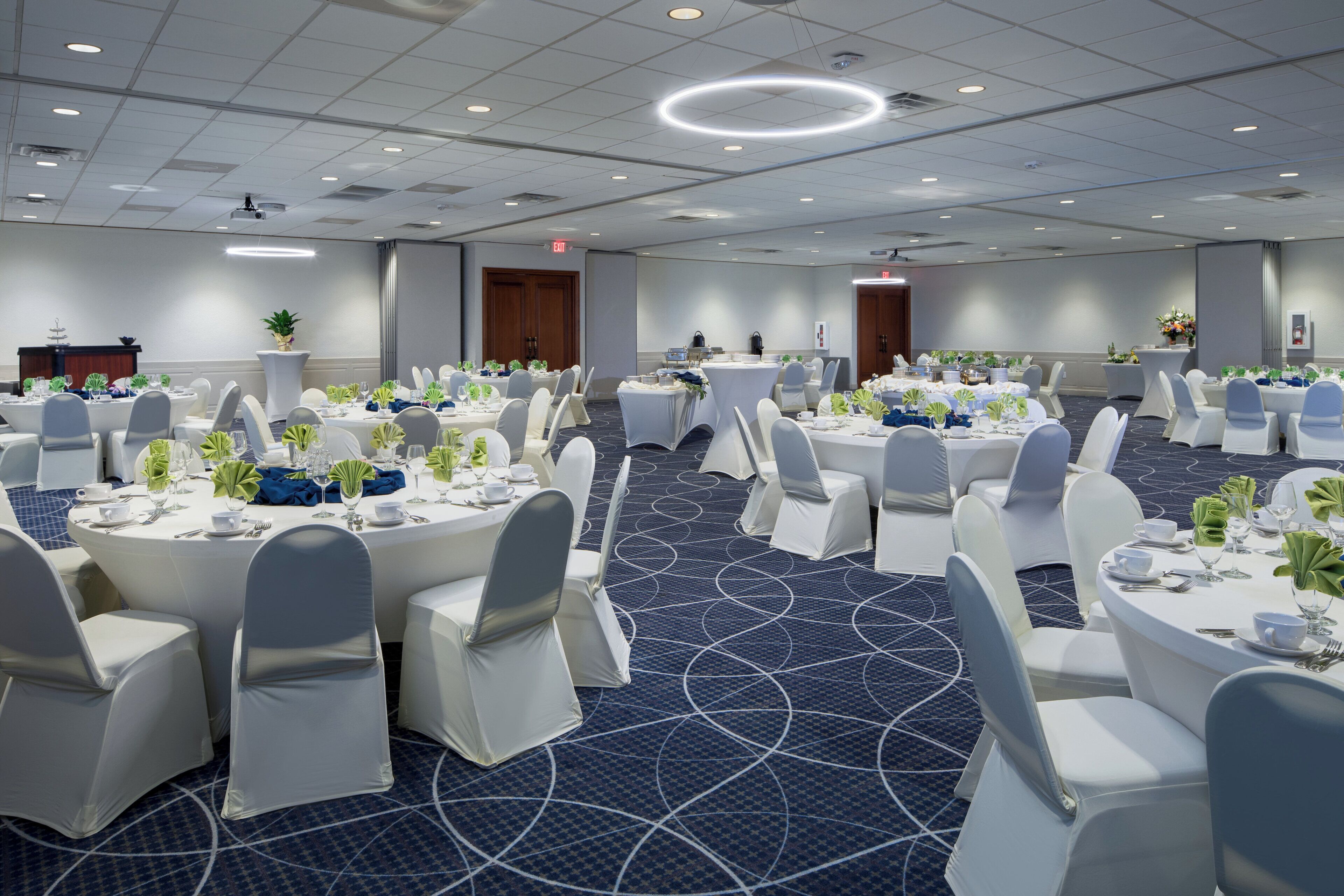 Une salle de conférence dotée de plusieurs tables rondes, de chaises blanches et d’un tapis bleu orné d’un motif circulaire.