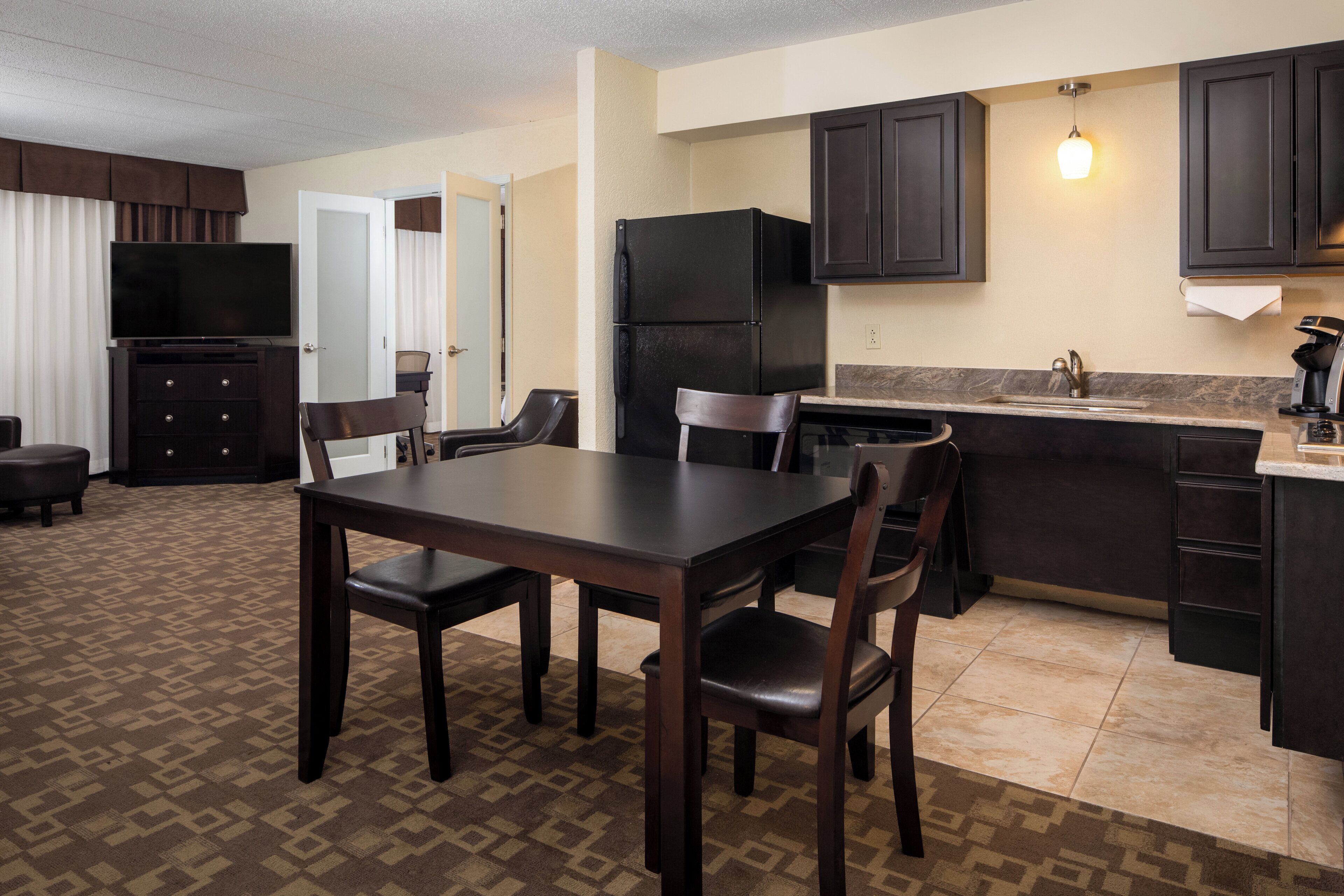 A compact hotel room with a dining area, kitchenette, and a television.