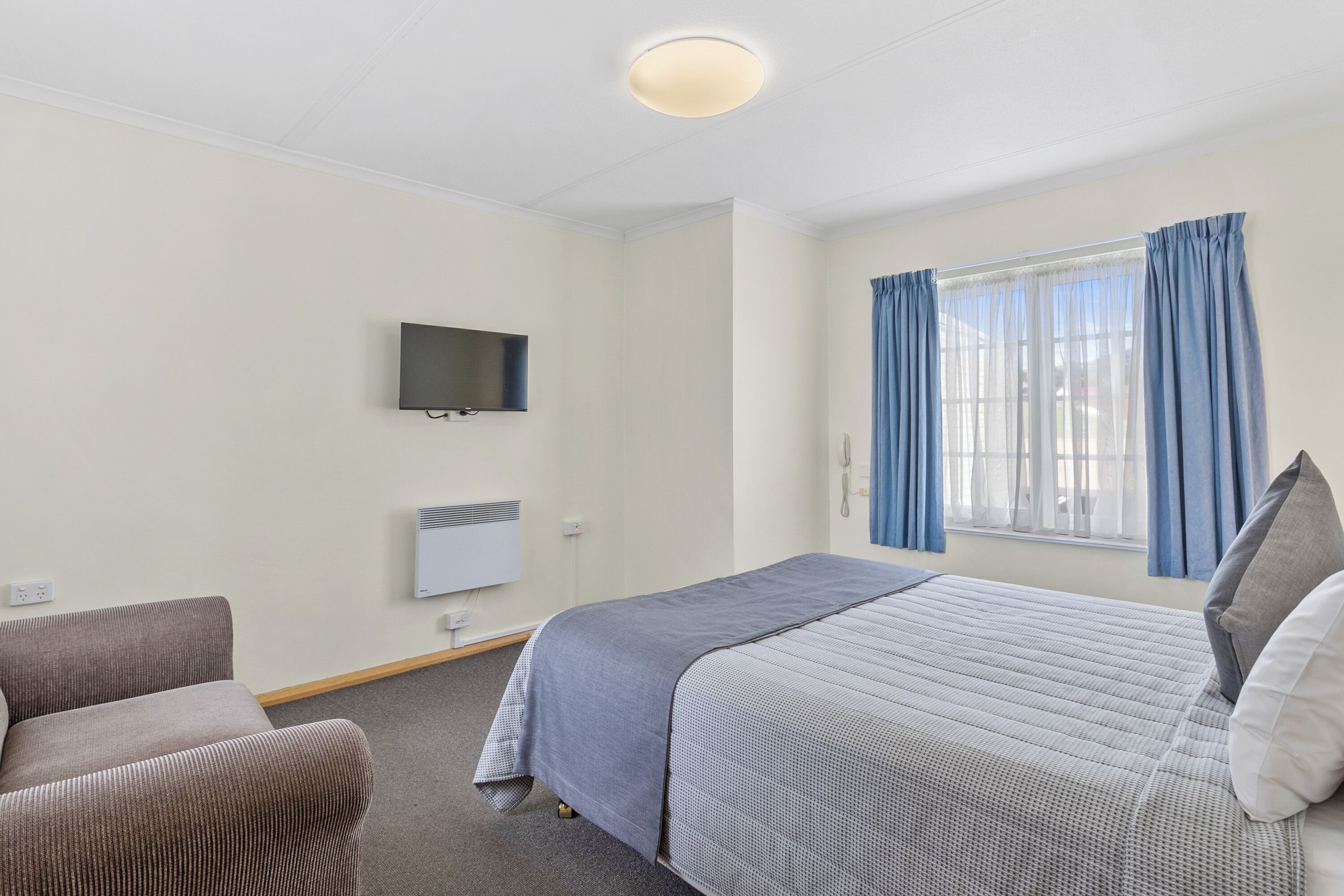 Habitació d'hotel amb un llit, una televisió penjada a la paret i una finestra amb cortines.