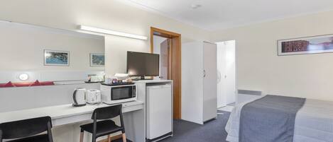 A hotel room with a bed, a desk with a computer, a microwave, and a refrigerator.