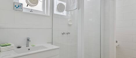 A modern bathroom with a white sink, a glass shower enclosure, and a window with a circular mirror.