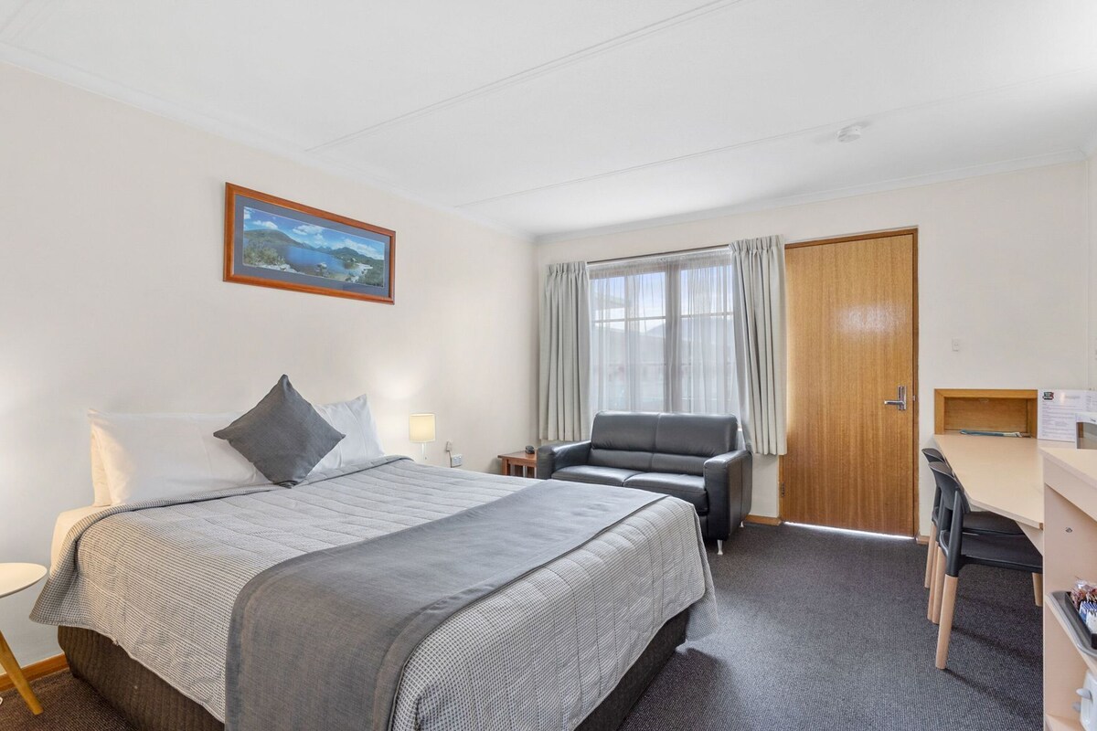 A hotel room with a bed, a desk, a chair, and a window with curtains.
