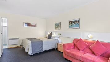 A hotel room with a bed, a red sofa, a bedside table with a lamp, and three framed pictures on the wall.