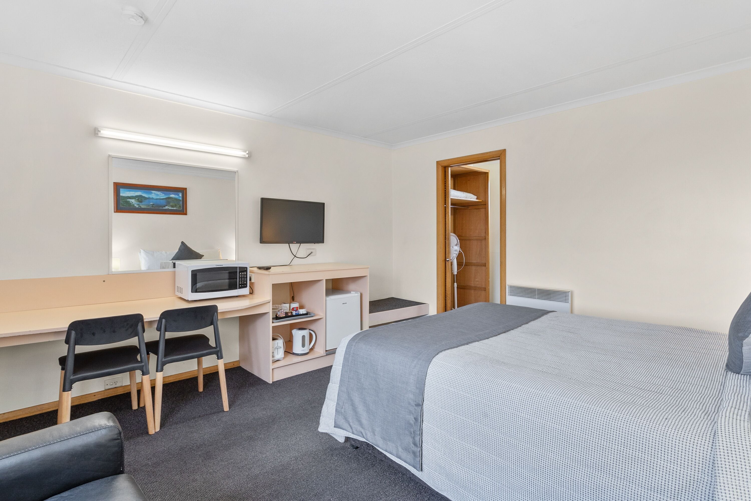 A hotel room with a bed, desk, chairs, a television, a microwave, and a wardrobe.