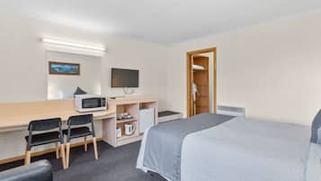 Quarto de hotel com cama, escrivaninha, cadeiras, televisão, micro-ondas e guarda-roupa.