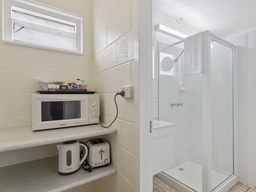 Een badkamer met een douche, een magnetron, een broodrooster en een waterkoker op een aanrecht.