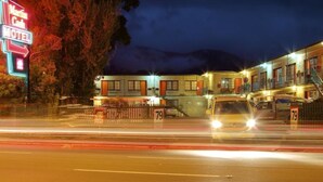 A motel with a neon sign, a fenced parking area, and a mountain in the background. - Martin Cash Motel (Moonah)
