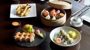 A variety of sushi dishes on a wooden table, accompanied by chopsticks, a bowl of dipping sauce, and a small bowl of wasabi.