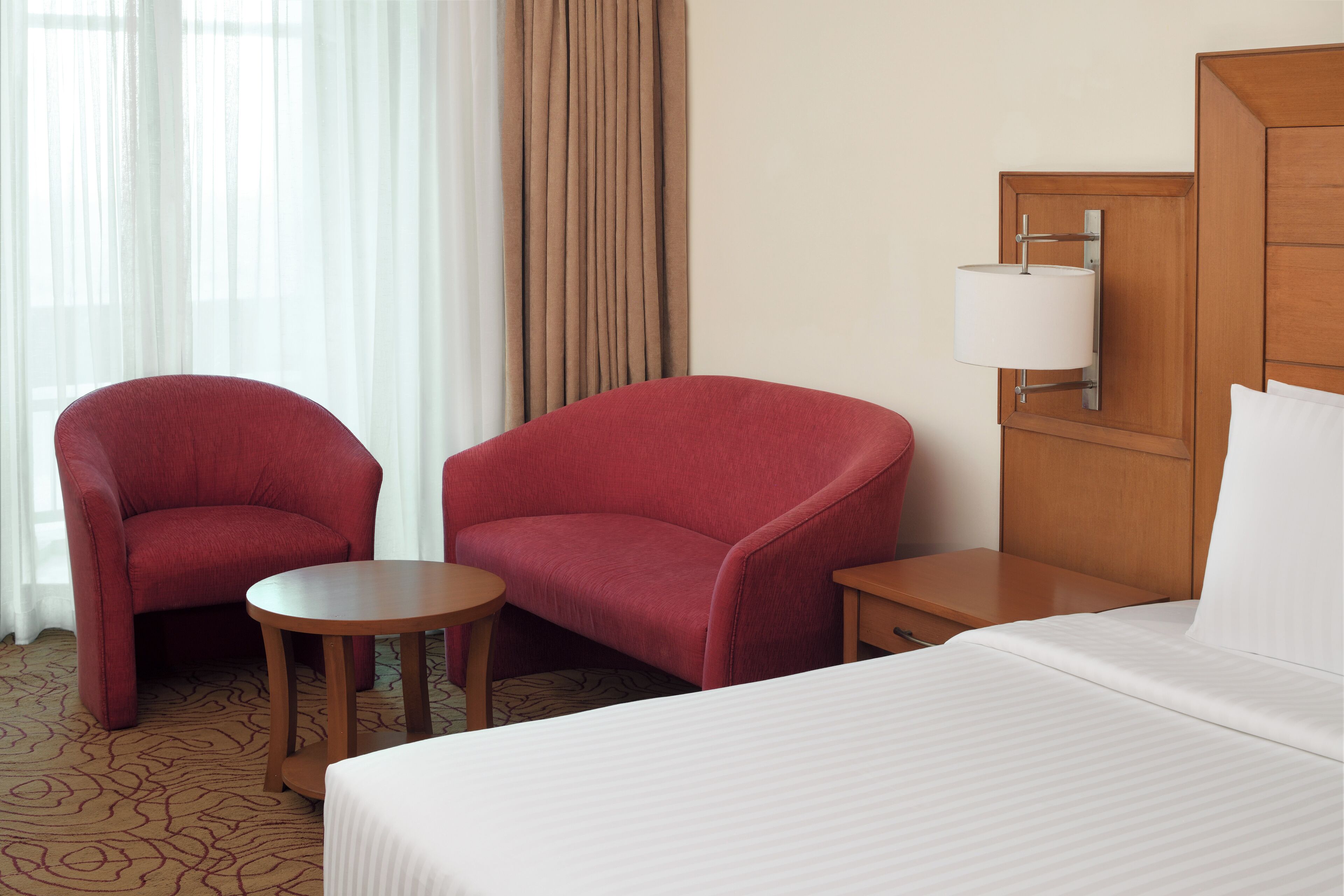 Ein Hotelzimmer mit einem Bett, zwei Sesseln, einem kleinen Tisch, einem Nachttisch und einer Lampe.